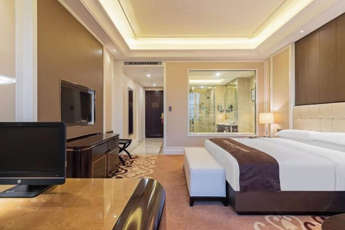 Quarto de hotel com cama, escrivaninha com um laptop, televisão e espelho.