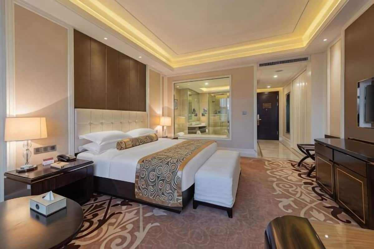 Quarto de hotel com uma cama grande, mesas de cabeceira, uma escrivaninha, uma cadeira, uma televisão e um espelho.