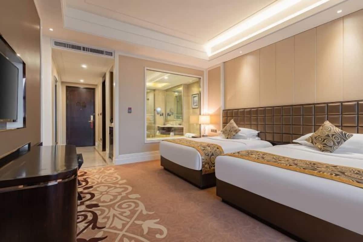 Quarto de hotel com duas camas, uma televisão, uma escrivaninha e um espelho.