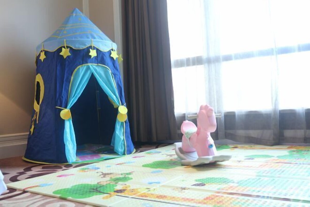 Une tente bleue ornée d’étoiles, un cheval à bascule rose et un tapis de jeu aux couleurs vives.