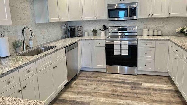 A modern kitchen with white cabinets, stainless steel appliances, and a granite countertop. - Modern 2bd 2ba - Near I75, No Steps, Free Wifi (Richmond)