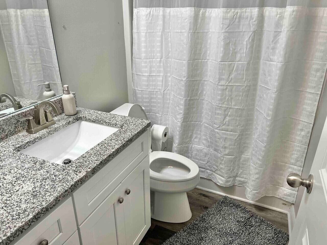 A bathroom with a granite countertop sink, a toilet, and a shower curtain.