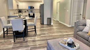A modern kitchen with white cabinets, a dining area with a round table and chairs, and a living room with a grey sofa and a coffee table. - Modern 2bd 2ba - Near I75, No Steps, Free Wifi (Richmond)