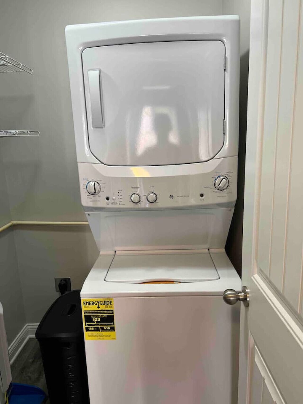 A front-loading white washer and dryer unit with a control panel, ENERGY GUIDE sticker, and a black trash bin beside it.