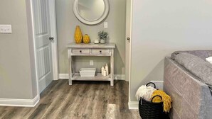 A hallway with a white door, a round mirror, a white console table with decorative items, and a gray sofa. - Modern 2bd 2ba - Near I75, No Steps, Free Wifi (Richmond)