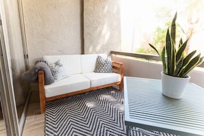 A balcony with a white sofa, patterned rug, and a potted plant.