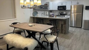 A modern kitchen with a central island, white cabinetry, stainless steel appliances, and a dining area with a wooden table and fluffy chairs. - Modern Getaway in Downtown Bozeman! (Bozeman)