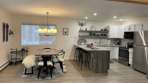 A modern kitchen with a central island, stainless steel appliances, and a dining area with a wooden table and chairs. - Modern Getaway in Downtown Bozeman! (Bozeman)