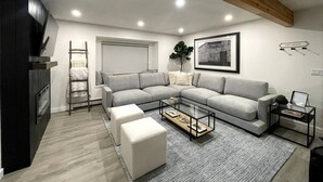 A modern living room with a grey sectional sofa, a glass coffee table, and a ladder against the wall. - Modern Getaway in Downtown Bozeman! (Bozeman)