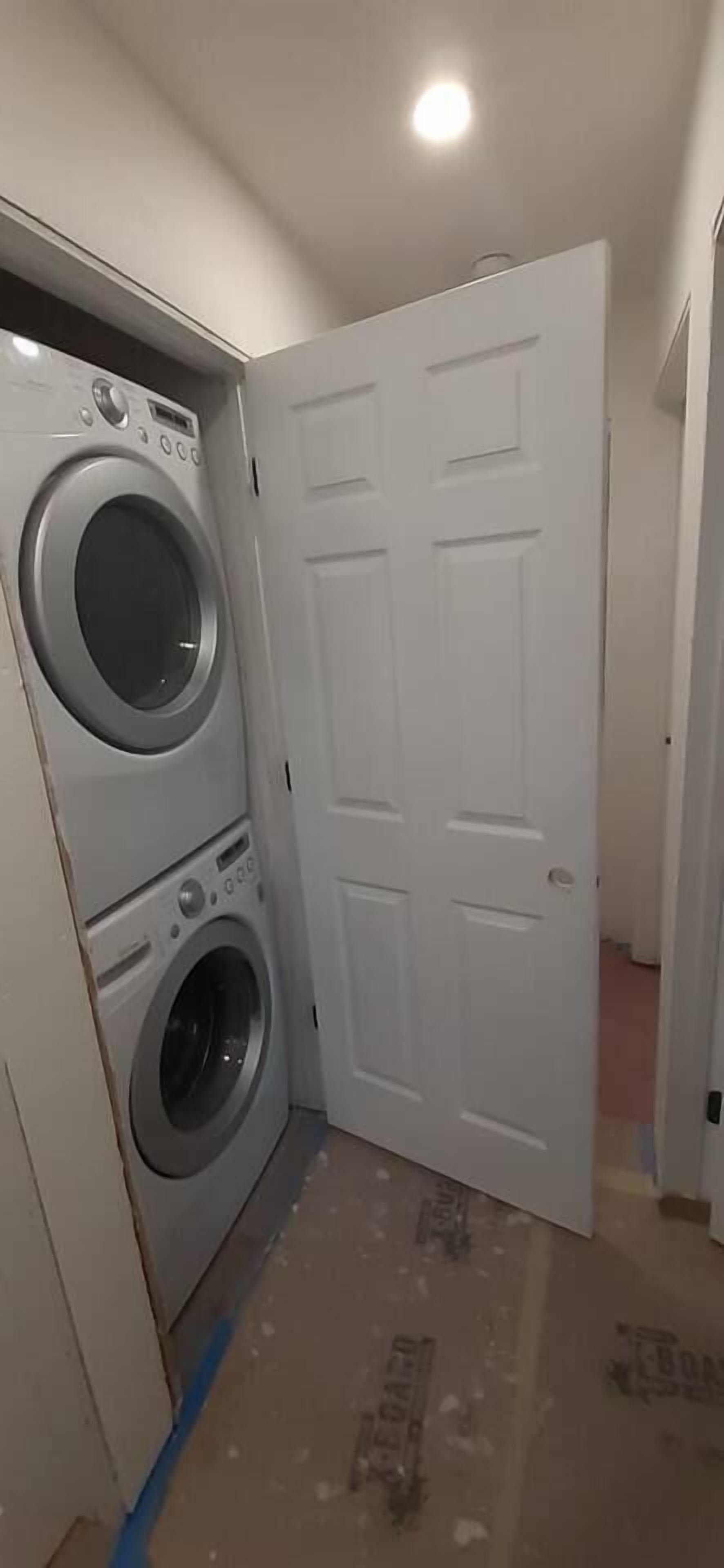 Une buanderie équipée d’un lave-linge et d’un sèche-linge, avec une porte blanche et un sol partiellement recouvert.