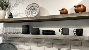 A kitchen with a wooden shelf holding black and brown mugs, a white plate with a black design, and a potted plant. - Modern Getaway in Downtown Bozeman! (Bozeman)