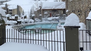 A snow-covered outdoor pool area with lounge chairs and a stone building in the background. - Lift Base Village - Grand Lodge King Bedroom Suite (Mount Crested Butte)