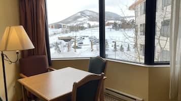 A hotel room with a large window offering a view of a snowy landscape and a mountain.