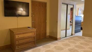 A hotel room with a bed, a wooden dresser, a television mounted on the wall, a door, and a sliding glass door leading to a balcony.