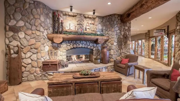 A stone-walled living room with a fireplace, wooden furniture, and a stone shelf. - Lift Base Village - Grand Lodge King Bedroom Suite (Mount Crested Butte)