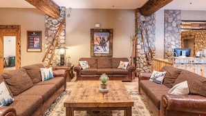 A cozy living room with a wooden coffee table, two brown leather sofas, and stone walls. - Lift Base Village - Grand Lodge King Bedroom Suite (Mount Crested Butte)
