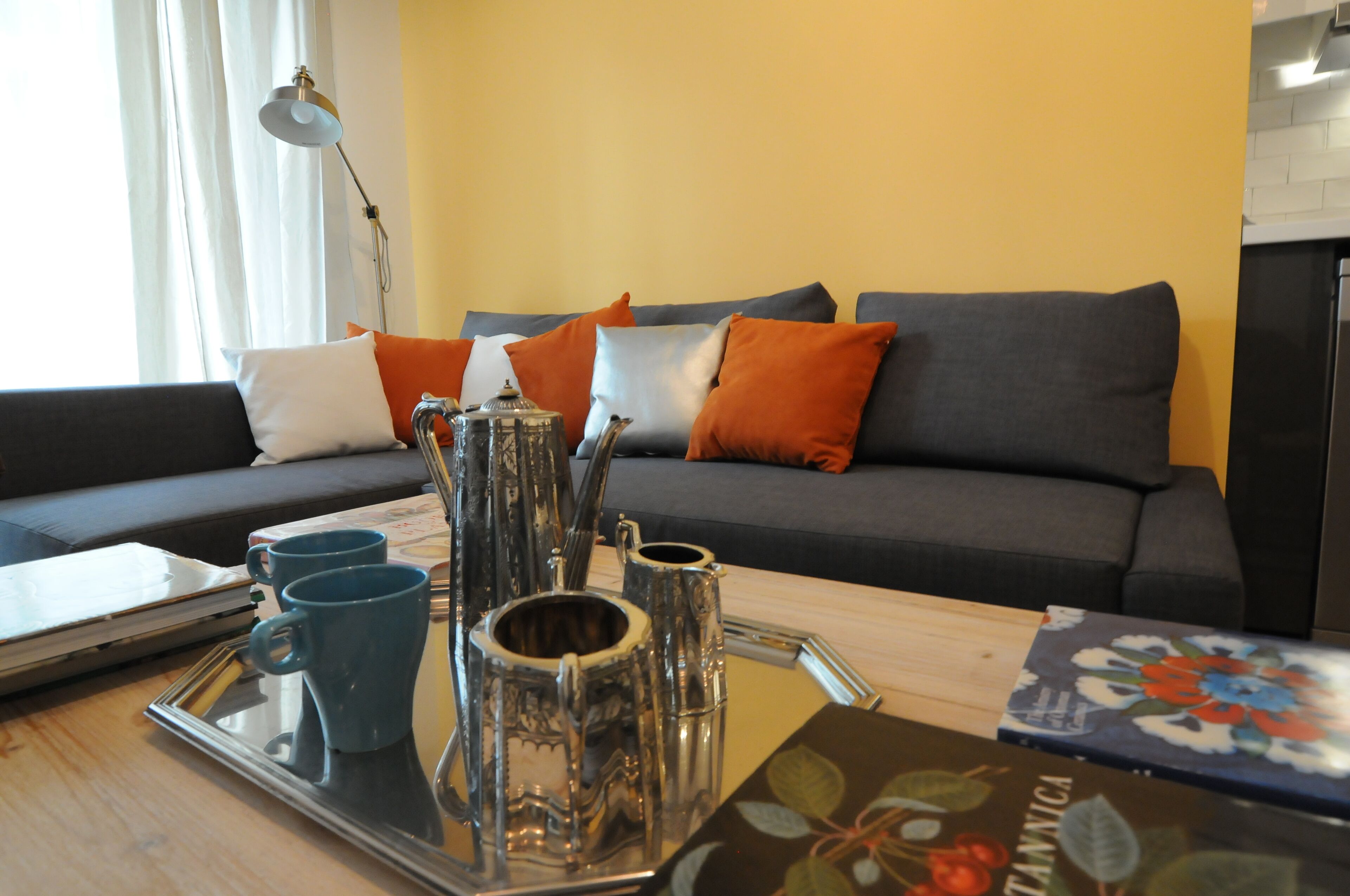 Un salon moderne avec un canapé, une table basse sur laquelle se trouve un plateau rempli de tasses, et une lampe décorative.