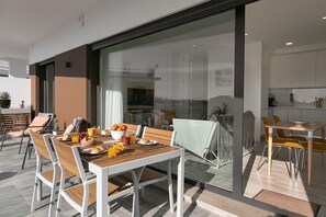 A modern dining area with a wooden table and chairs, a glass partition, and a view of the kitchen.