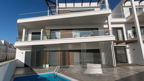 Un edificio moderno de varios pisos con piscina en la azotea, balcones y una puerta de cristal que dice "EDIFIOU A BICA".