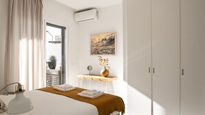Una habitación de hotel moderna con una cama, una mesita de noche con lámpara, una planta en maceta y un amplio armario.