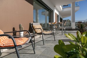 A modern outdoor patio with metal-framed chairs and orange-striped cushions, a glass table, and potted plants.