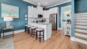 A modern kitchen with white cabinets, a stainless steel refrigerator, and a marble island with bar stools.