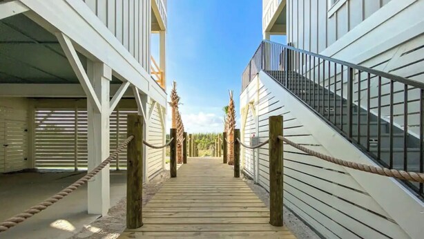 A wooden pathway leading to a building with white siding and a metal staircase.