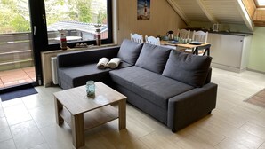 Ein modernes Wohnzimmer mit einem grauen Sofa, einem Holztisch und einem Essbereich mit Tisch für zwei Personen.