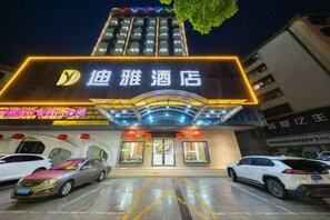 A hotel entrance with a neon sign, a parking lot, and cars parked in front.
