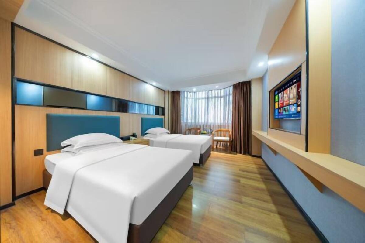 Une chambre d’hôtel avec deux lits, une télévision, un coin salon et une fenêtre avec des rideaux.