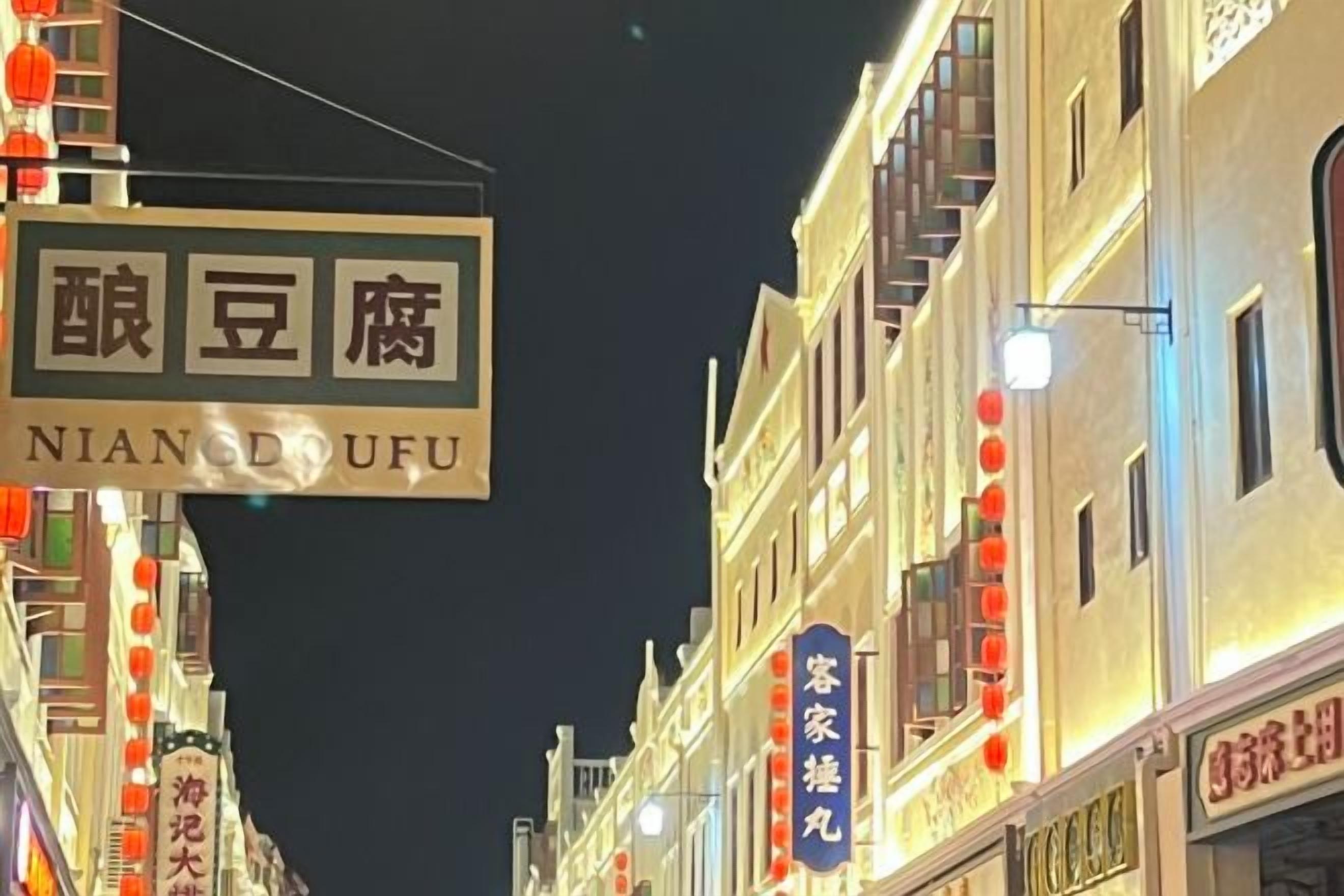 Straßenansicht mit beleuchteten Schildern, darunter eines für 'Nian Dofu' und ein weiteres für 'Coco'.