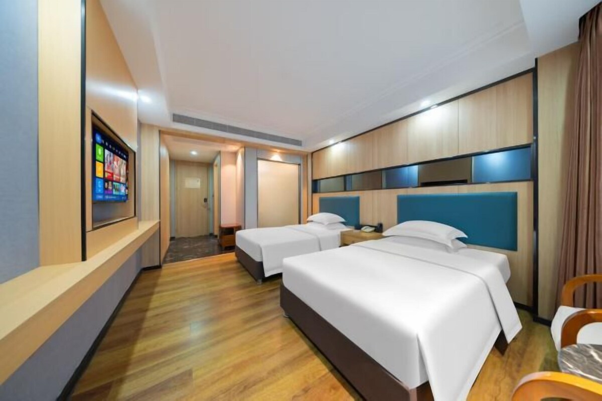 A hotel room with two beds, a TV, and a wooden floor.