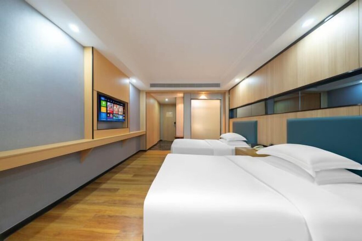 Une chambre d’hôtel avec deux lits, un téléviseur fixé au mur et un plancher en bois.