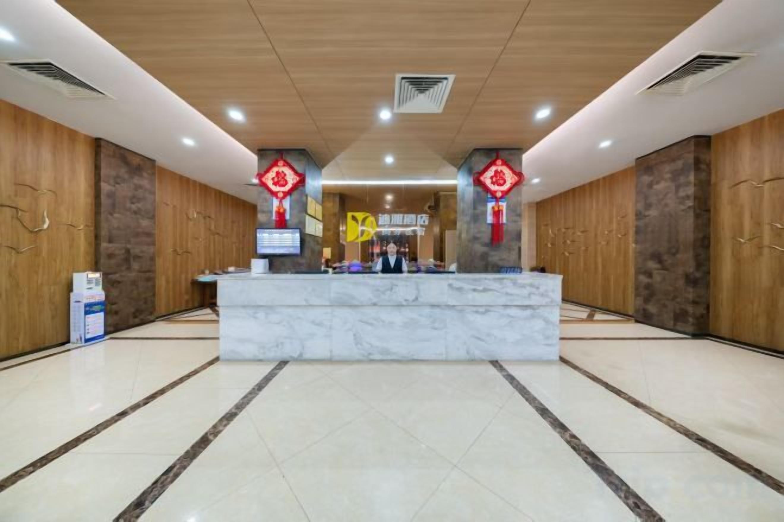 Zona de recepción de un hotel con mostrador de mármol, paredes de madera y detalles decorativos rojos.