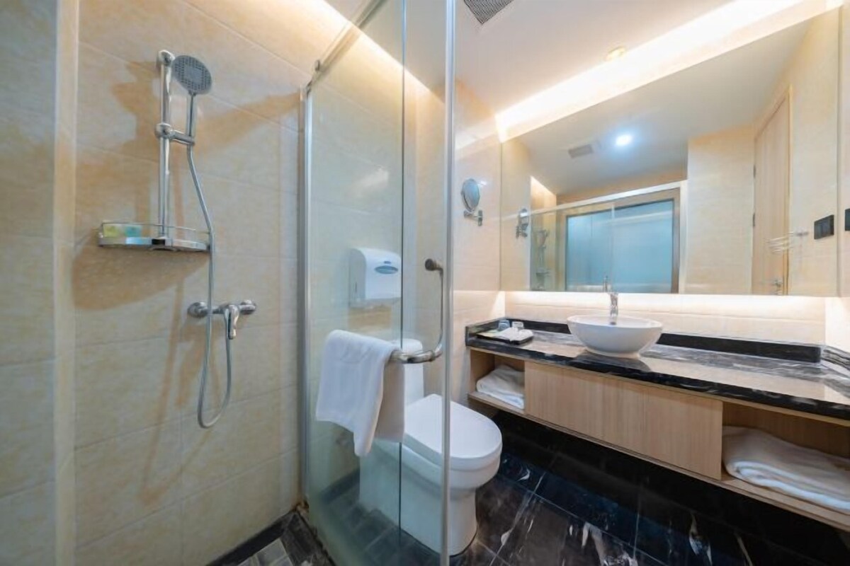 A modern bathroom with a glass-enclosed shower, a toilet, a sink with a marble countertop, and a mirror.