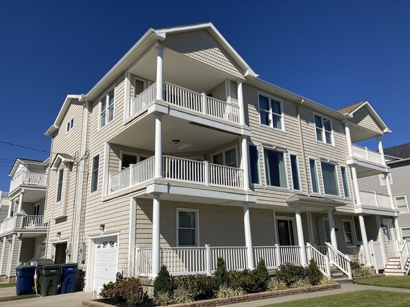 A multi-story residential building with a balcony on each floor, a front porch, and a driveway.