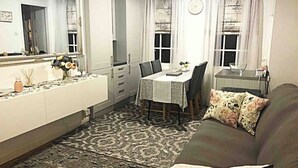 Un salon avec un tapis à motifs, un canapé agrémenté de coussins à fleurs, une table à manger avec des chaises et un grand miroir.