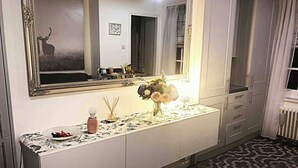 Une chambre d’hôtel avec un grand miroir, un vase décoratif rempli de fleurs, une petite table sur laquelle se trouve une assiette de nourriture et un tapis à motifs.