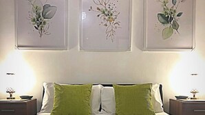 Un lit bien fait, avec une literie verte et blanche, flanqué de deux tables de chevet sur lesquelles reposent des lampes, et trois reproductions botaniques encadrées accrochées au mur au-dessus.