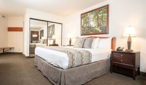 Relax in comfort with a large bed, nightstand, and mirror, complemented by a beautiful landscape painting and a small table.