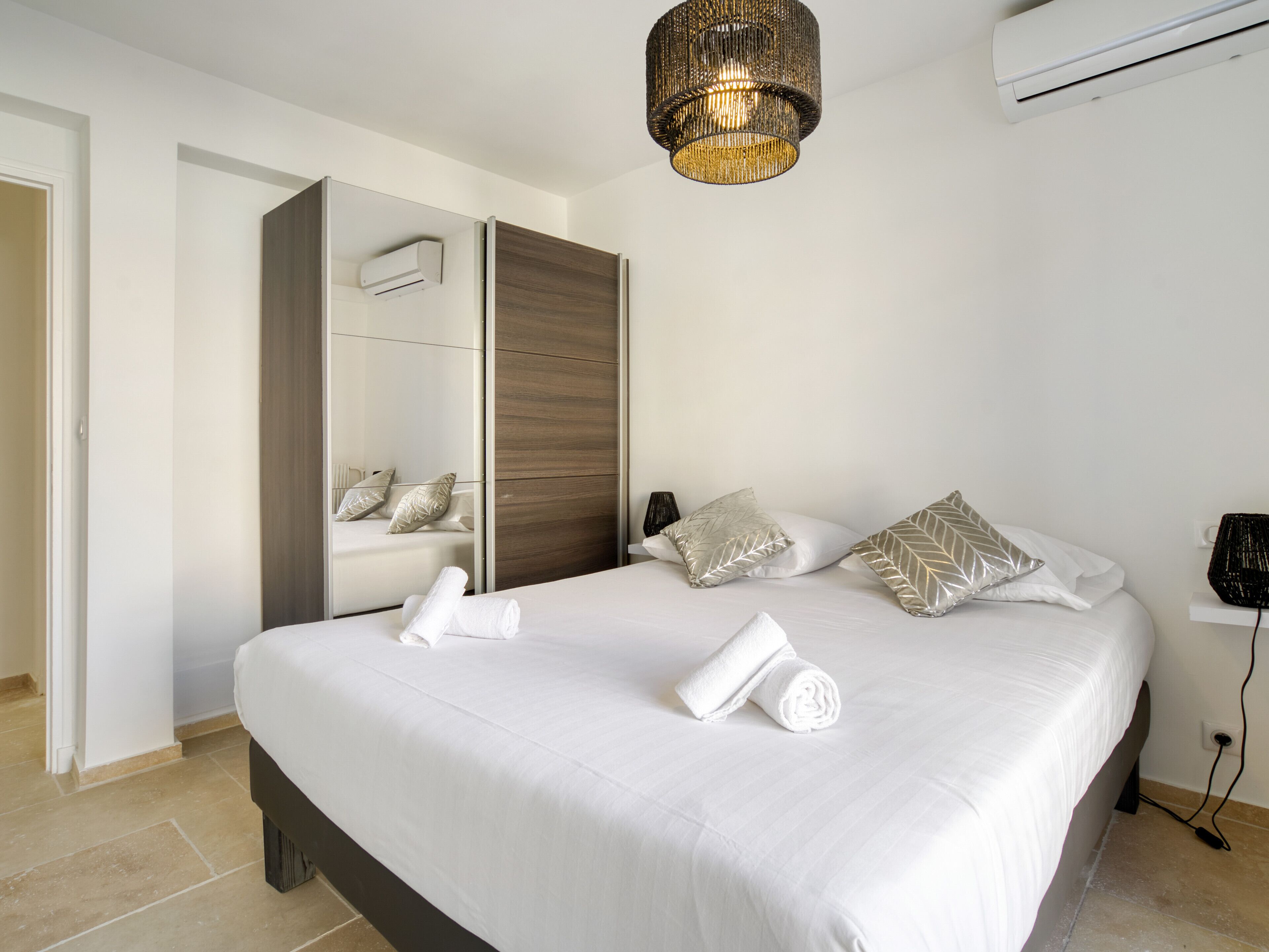 A modern bedroom with a large bed, a wardrobe, an air conditioning unit, and a hanging light fixture.