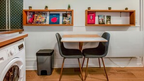 A kitchen with a washing machine, a trash bin, a table with two chairs, and shelves with books and small plants. - Appartement des Bergères - Welkeys (Paris)
