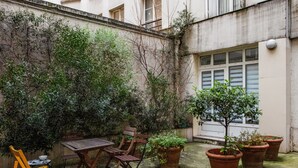 A courtyard with a wooden table and chairs, potted plants, and a small tree. - Appartement des Bergères - Welkeys (Paris)