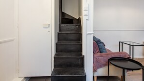A staircase leading to a room with a white door, a small round table, and a chair with a pink blanket. - Appartement des Bergères - Welkeys (Paris)