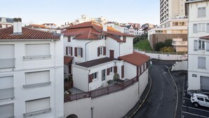 Une rue étroite, bordée de bâtiments des deux côtés, avec des balcons et des toits recouverts de tuiles rouges.