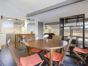 Une cuisine moderne avec un coin repas comprenant une table ronde en bois et des chaises dotées de coussins orange.