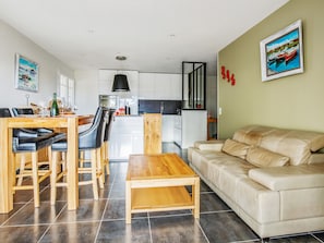 Un salon moderne avec un canapé beige, une table basse en bois et un coin repas comprenant une table en bois et des chaises en cuir noir.