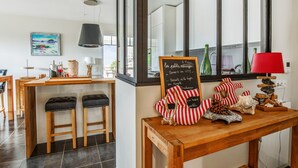 A modern kitchen with wooden stools, a chalkboard menu, and a view of the outdoors through large windows. - Appartement des Asphodèles - Welkeys (La Teste-de-Buch)