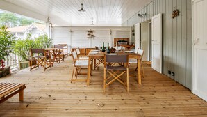 A covered patio with wooden flooring, a dining table set with chairs, and a view of a house in the background. - Appartement des Asphodèles - Welkeys (La Teste-de-Buch)