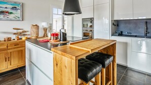 A modern kitchen with white cabinets, a wooden island, and a hanging light fixture. - Appartement des Asphodèles - Welkeys (La Teste-de-Buch)
